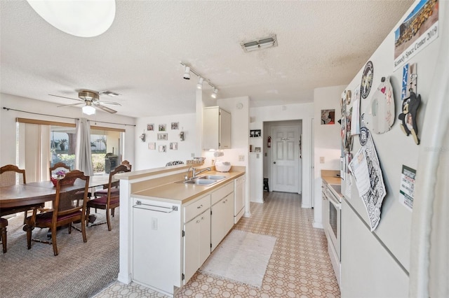 kitchen featuring a peninsula, white appliances, a sink, visible vents, and light countertops