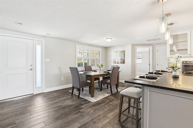 dining space with dark wood-style floors, baseboards, visible vents, a toaster, and a textured ceiling