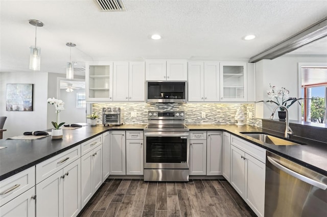 kitchen featuring visible vents, a peninsula, a sink, stainless steel appliances, and backsplash