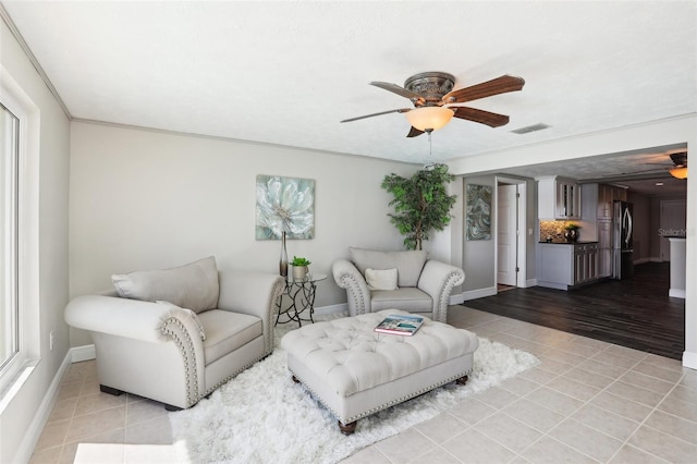 living room with light tile patterned flooring, a ceiling fan, visible vents, and baseboards