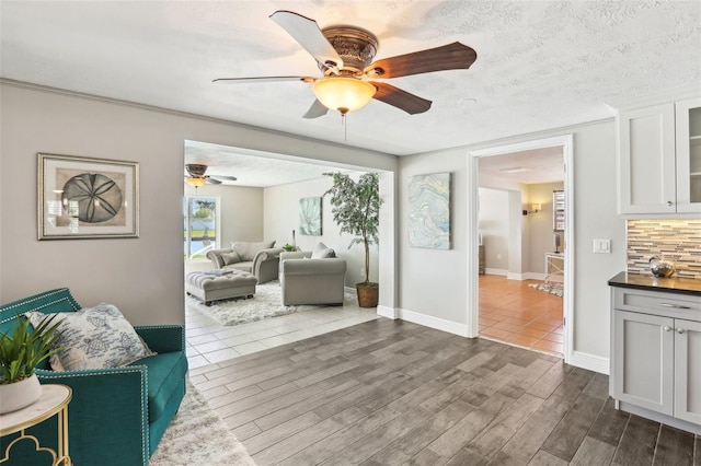 living room with dark wood finished floors, a textured ceiling, baseboards, and ceiling fan