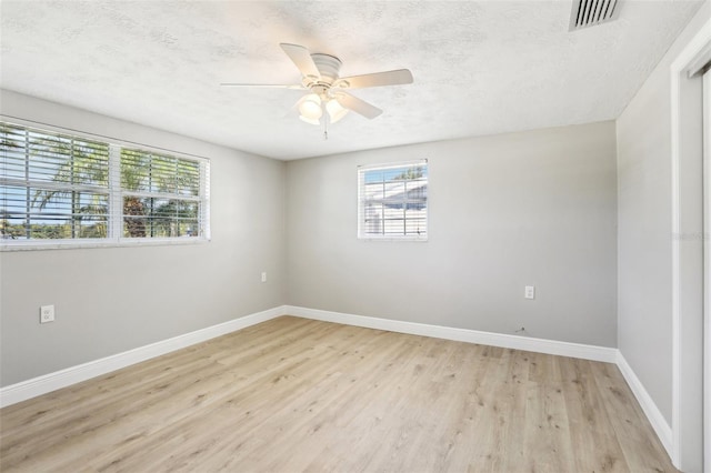 empty room with baseboards, visible vents, light wood finished floors, ceiling fan, and a textured ceiling