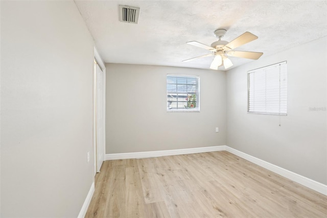 empty room with visible vents, light wood-style flooring, a textured ceiling, and baseboards