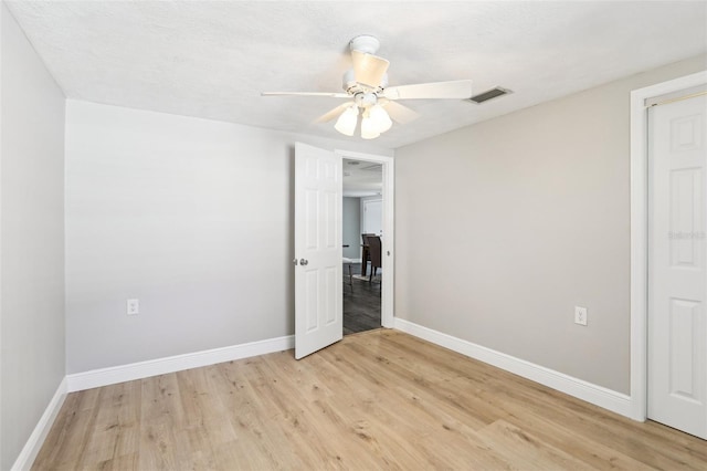 empty room with a ceiling fan, light wood-style flooring, baseboards, and visible vents