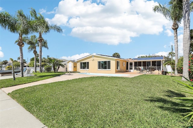 rear view of house with stucco siding, a patio, a yard, a sunroom, and solar panels