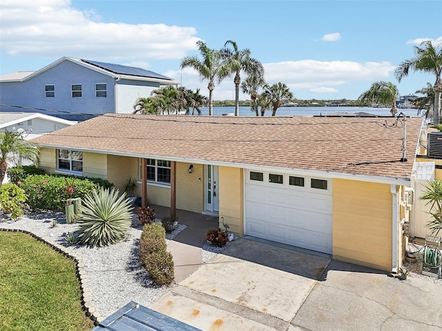 ranch-style house featuring an attached garage, concrete driveway, roof with shingles, and a water view