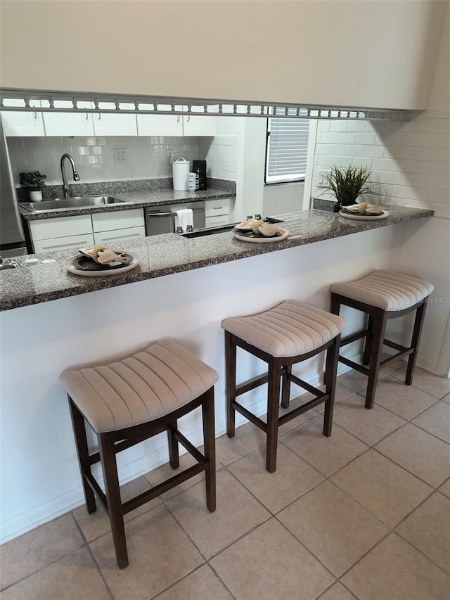 kitchen featuring a breakfast bar, stainless steel dishwasher, backsplash, and a sink