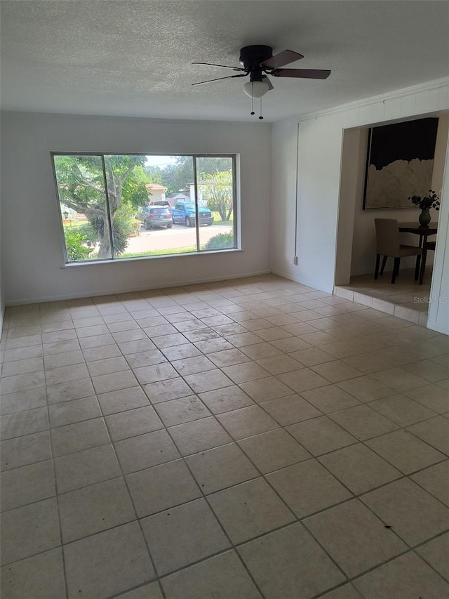 empty room with light tile patterned floors, ceiling fan, and a textured ceiling