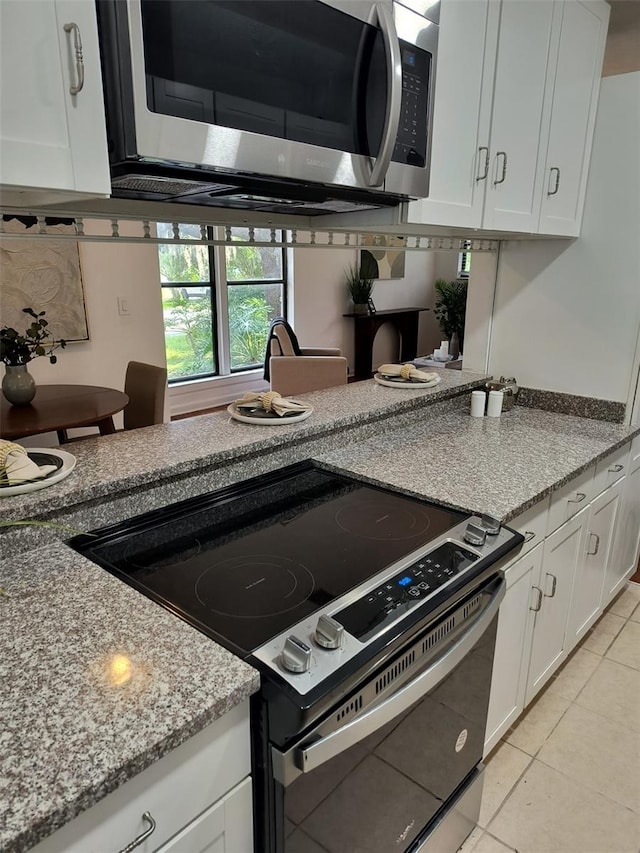 kitchen featuring light tile patterned floors, white cabinets, light stone countertops, electric range oven, and stainless steel microwave