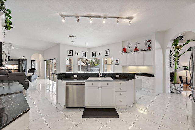 kitchen featuring arched walkways, open floor plan, white cabinets, a sink, and dishwasher