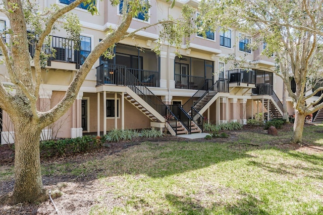 back of house featuring central air condition unit, a sunroom, stairs, a lawn, and stucco siding