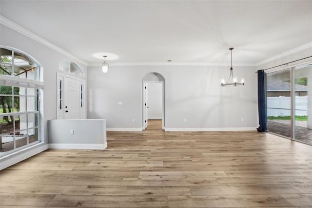 interior space featuring arched walkways, light wood-style flooring, an inviting chandelier, ornamental molding, and baseboards