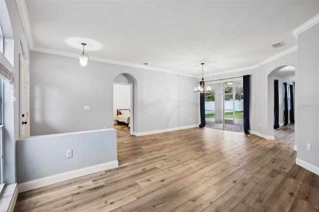 empty room with arched walkways, wood finished floors, visible vents, baseboards, and ornamental molding