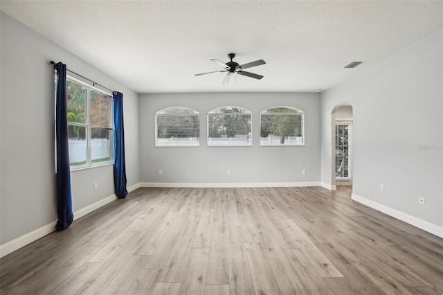 unfurnished room with light wood-type flooring, a healthy amount of sunlight, visible vents, and arched walkways