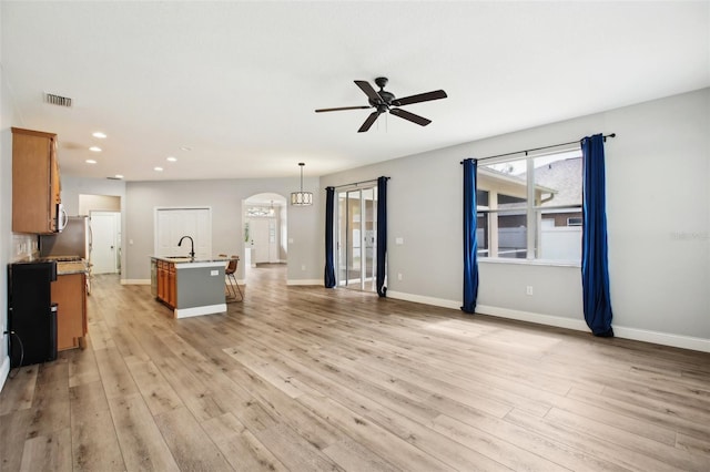 unfurnished living room with baseboards, light wood-style flooring, arched walkways, and a ceiling fan