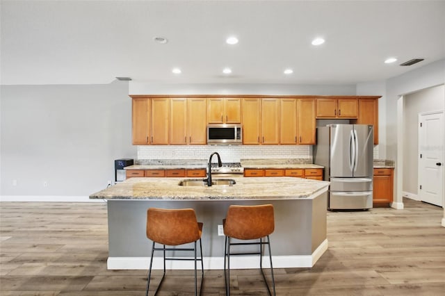 kitchen with a sink, light wood-style flooring, stainless steel appliances, and backsplash