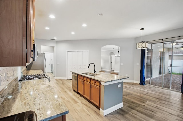 kitchen with arched walkways, stainless steel appliances, a sink, light wood-type flooring, and brown cabinets