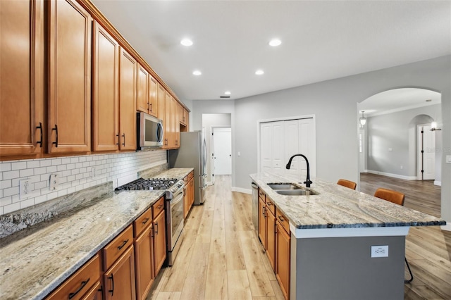 kitchen featuring arched walkways, light wood-style flooring, stainless steel appliances, a sink, and a kitchen breakfast bar