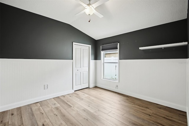 unfurnished room with a wainscoted wall, a ceiling fan, vaulted ceiling, and wood finished floors