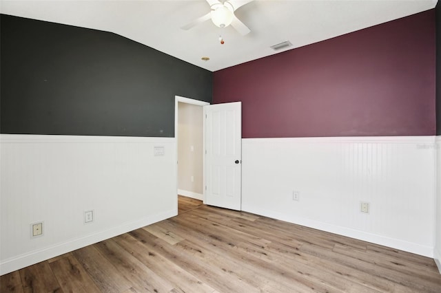 empty room featuring ceiling fan, lofted ceiling, a wainscoted wall, wood finished floors, and visible vents