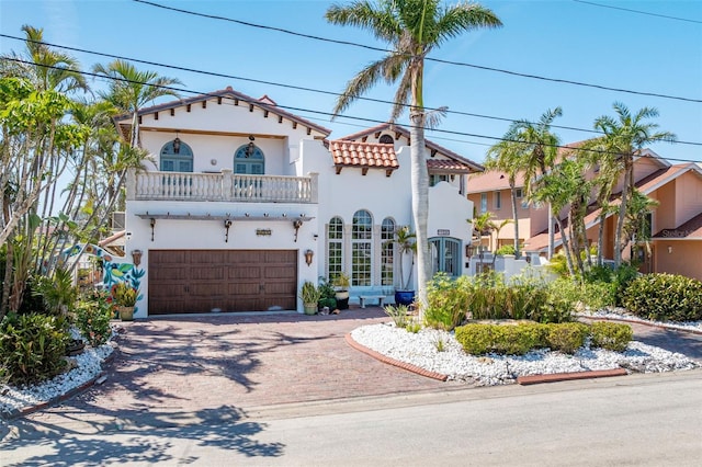 mediterranean / spanish-style home featuring decorative driveway, a tile roof, stucco siding, a balcony, and a garage