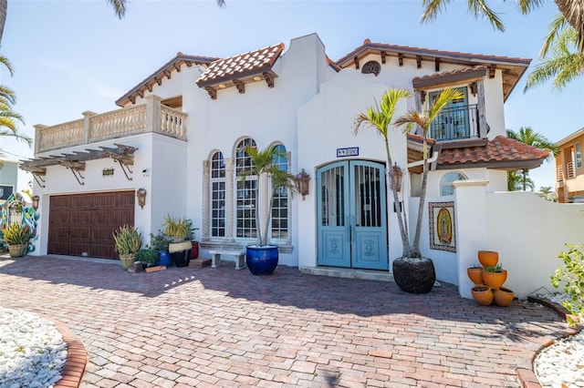 mediterranean / spanish house featuring a balcony, an attached garage, a tiled roof, and french doors