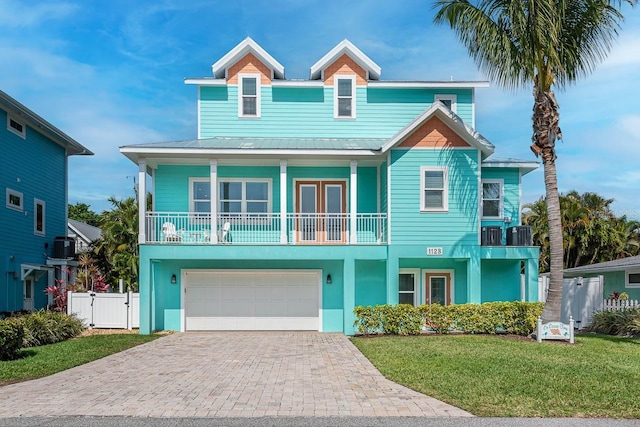 coastal inspired home featuring metal roof, fence, decorative driveway, a gate, and a front lawn