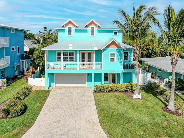 coastal home with decorative driveway, a front yard, a gate, fence, and a balcony