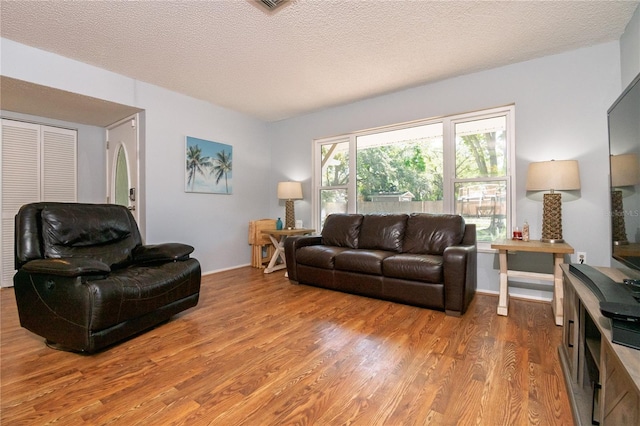 living room with baseboards, a textured ceiling, and light wood-style flooring