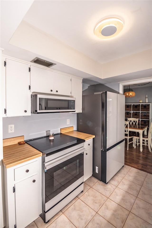 kitchen with white microwave, visible vents, freestanding refrigerator, range with electric cooktop, and white cabinets