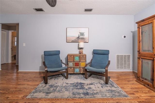 sitting room with visible vents, a textured ceiling, and wood finished floors