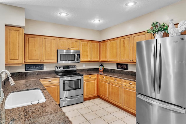 kitchen featuring dark stone counters, appliances with stainless steel finishes, a textured ceiling, a sink, and light tile patterned flooring