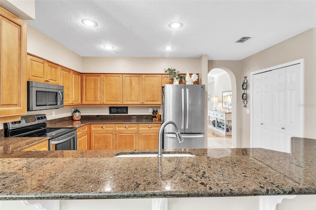 kitchen featuring visible vents, stainless steel appliances, a sink, and dark stone counters