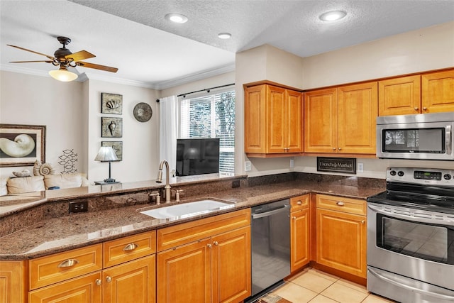 kitchen featuring dark stone counters, ornamental molding, stainless steel appliances, a sink, and light tile patterned flooring