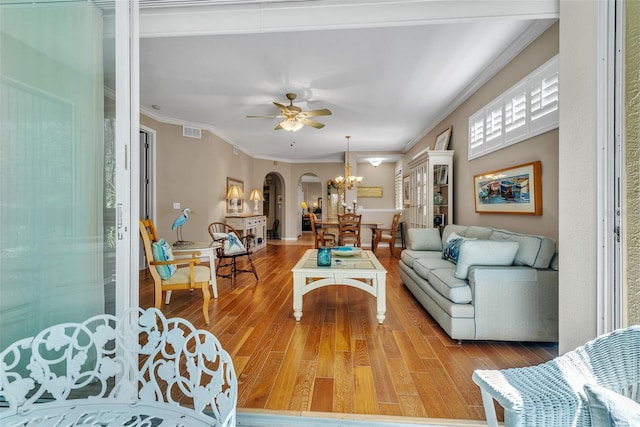 living room featuring arched walkways, ceiling fan with notable chandelier, wood finished floors, visible vents, and ornamental molding