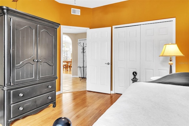 bedroom featuring arched walkways, a closet, visible vents, light wood-type flooring, and baseboards