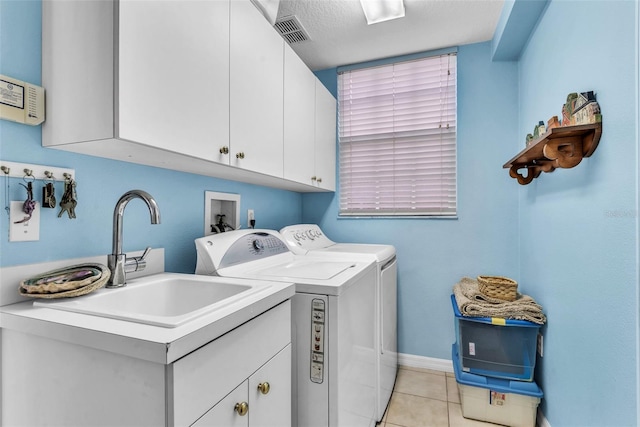 clothes washing area with cabinet space, light tile patterned floors, visible vents, washing machine and dryer, and a sink