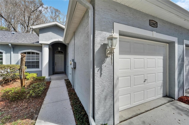 view of exterior entry with a garage and stucco siding