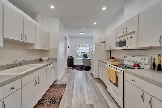 kitchen featuring light countertops, decorative backsplash, arched walkways, white appliances, and a sink