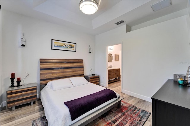 bedroom featuring visible vents, a raised ceiling, light wood-type flooring, and baseboards