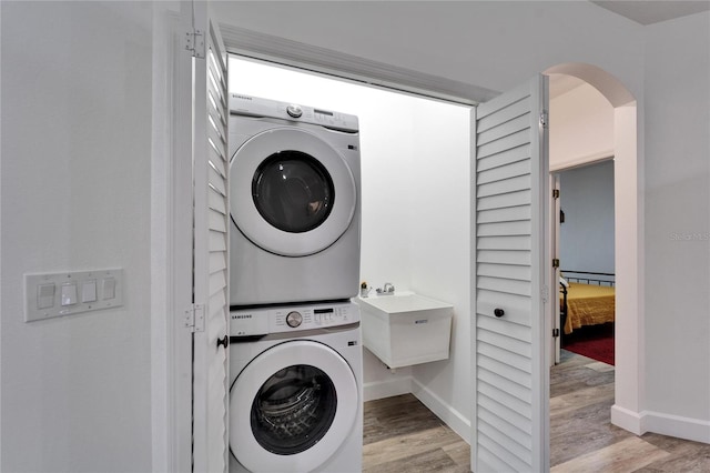 clothes washing area with baseboards, light wood finished floors, laundry area, and stacked washing maching and dryer