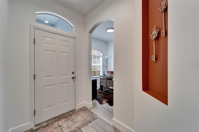 foyer entrance featuring baseboards, arched walkways, and light wood-style flooring