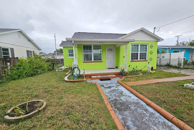 bungalow with a porch, fence, a front lawn, and roof with shingles