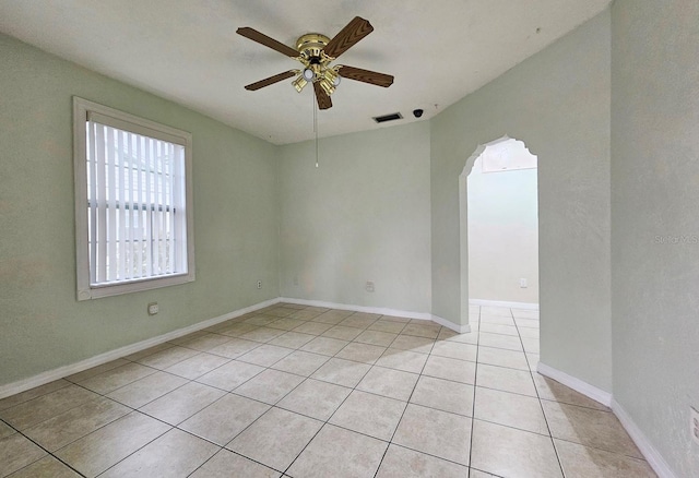 unfurnished room featuring light tile patterned floors, baseboards, visible vents, arched walkways, and a ceiling fan