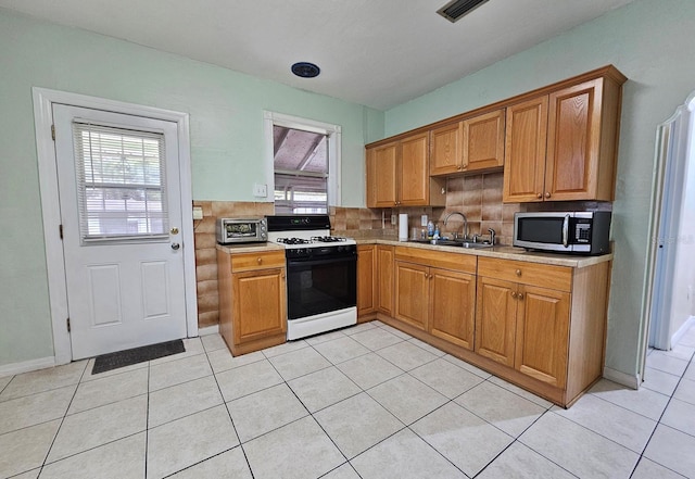 kitchen with visible vents, range with gas stovetop, stainless steel microwave, light countertops, and a sink