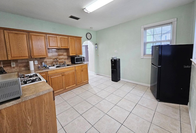 kitchen with arched walkways, stainless steel microwave, stove, freestanding refrigerator, and a sink