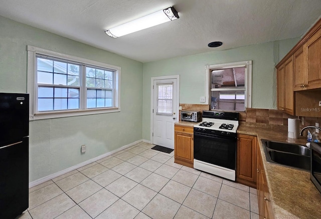 kitchen featuring light tile patterned floors, brown cabinetry, freestanding refrigerator, a sink, and gas range