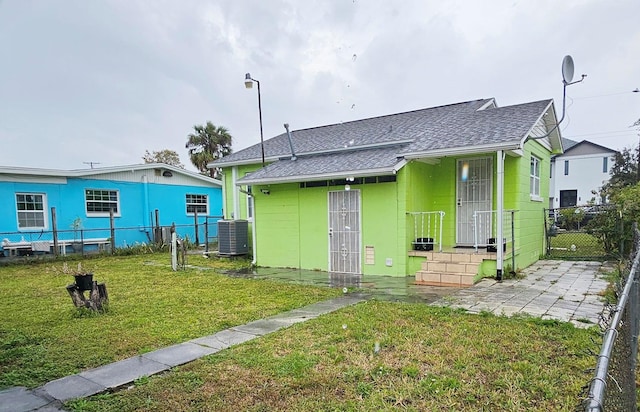 back of property with roof with shingles, a yard, central air condition unit, a gate, and fence