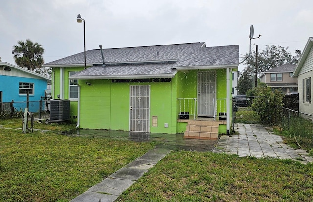 view of front of house featuring central AC, fence, roof with shingles, a gate, and a front lawn