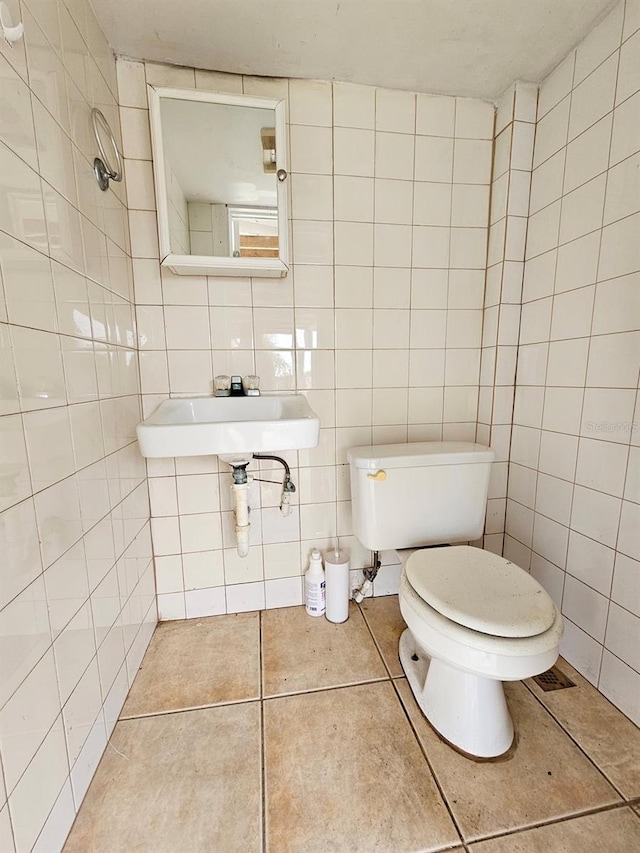 bathroom with a sink, tile walls, toilet, and tile patterned floors